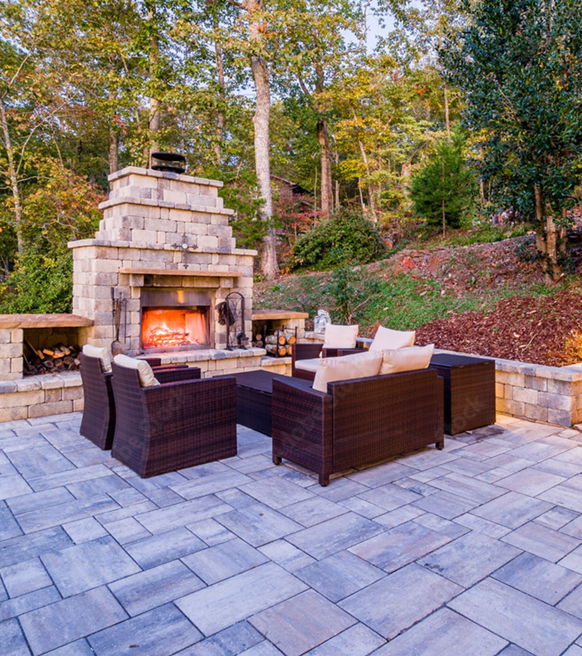 Luxurious outdoor patio with paved stone floor, a wood-fired pizza oven, and lush greenery in the background