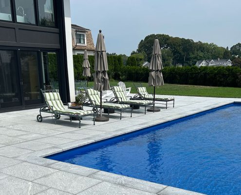 Stone patio by blue pool and lounge chairs