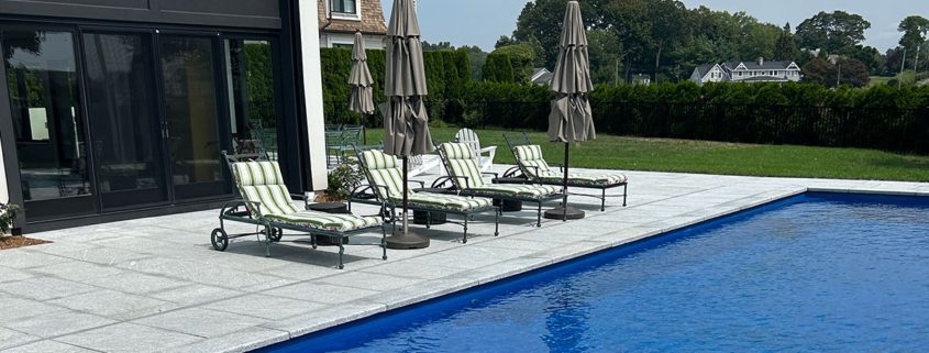 Stone patio by blue pool and lounge chairs