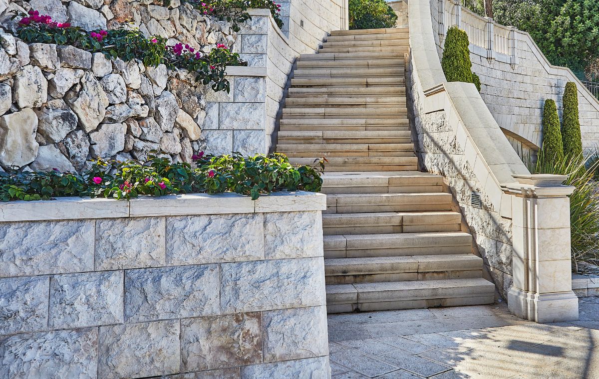 A stone staircase adorned with vibrant flowers and plants, set against a stone retaining wall in Chester, CT.