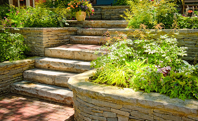 Custom stone retaining wall with steps ascending to a house, located in Chester, CT.