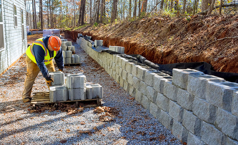 A man works on a stone retaining wall in Chester, CT, contributing to effective erosion control and landscape preservation.