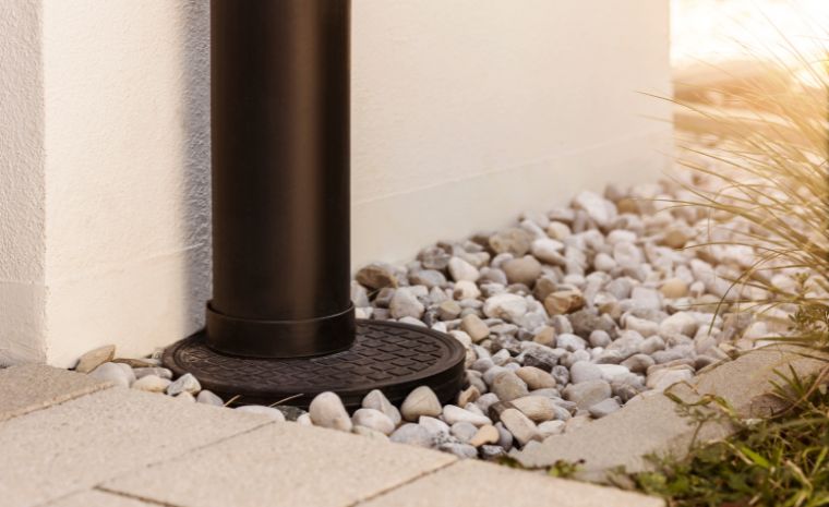 A black drainage pipe resting on gravel and rocks, highlighting efficient gutter downspout connections in Stonington, Connecticut.