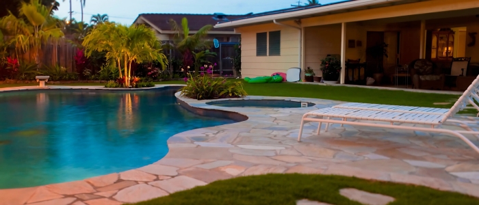 A picturesque backyard with a pool and lawn chairs on a stone deck, offering a relaxing atmosphere and design ideas.