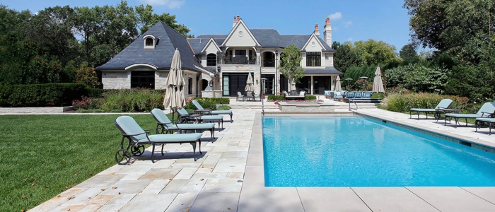 A large residence with a pool and lawn chairs, showcasing a stone pool deck designed by Elite Landscapes & Concrete.