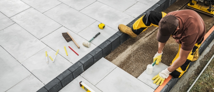 A worker installing tiles on the ground as part of the stone pool deck installation process.