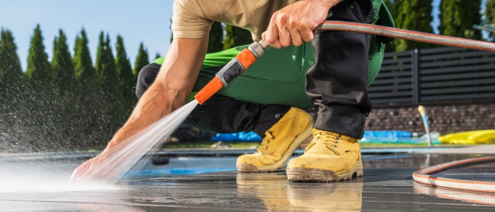 A man cleans a pool using a hose, showcasing maintenance tips for a stone pool deck.