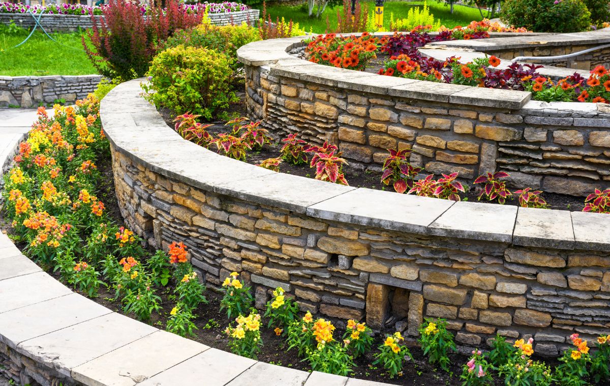 A stone wall adorned with vibrant flowers and plants, showcasing a retaining wall by a mason contractor in Branford, CT.
