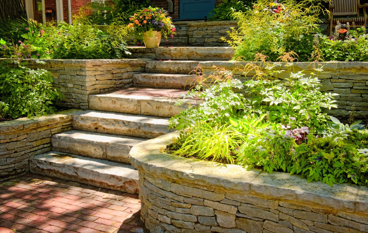A decorative stone retaining wall with lush plants and flowers, representing masonry services in Guilford, CT.