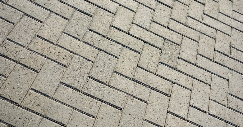 A close-up of a brick sidewalk with a man walking, illustrating the texture and design of paver materials.