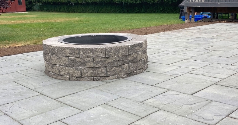 A stone fire pit on a patio, surrounded by outdoor seating, ideal for cozy gatherings in a backyard setting.