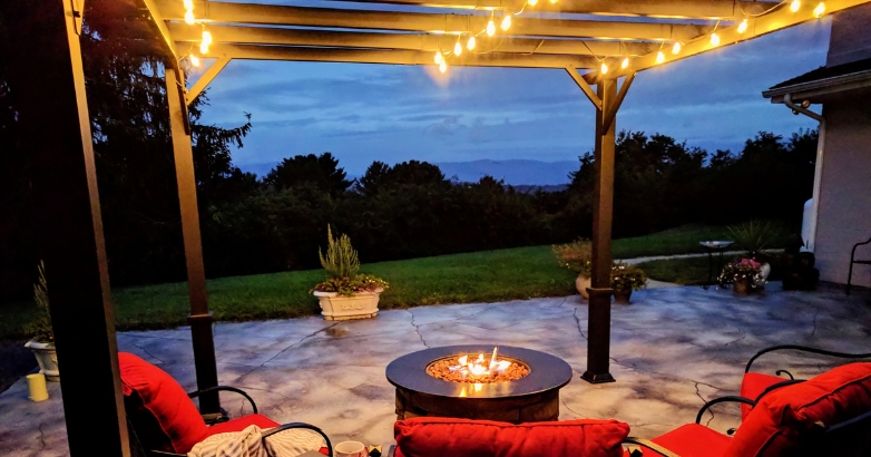 A fire pit flanked by red cushions and a gazebo, perfect for a backyard patio enhanced with decorative string lights.