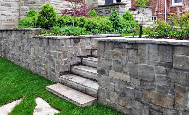 A stone retaining wall with steps ascending to a house, illustrating masonry construction techniques in Chester, CT.