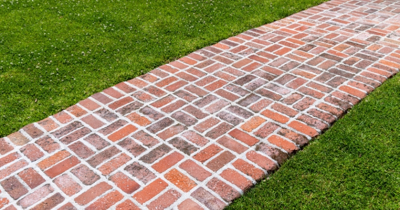 A brick pathway in a herringbone pattern surrounded by lush green grass, showcasing a front walkway design idea.