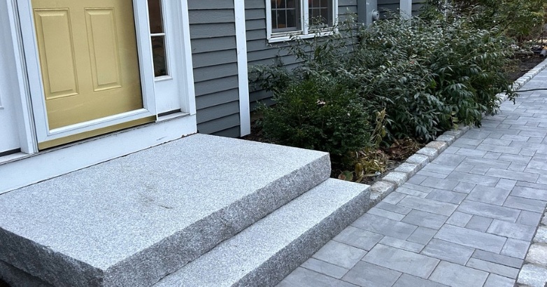 A granite slab walkway leads to a house showcasing an inviting entrance.
