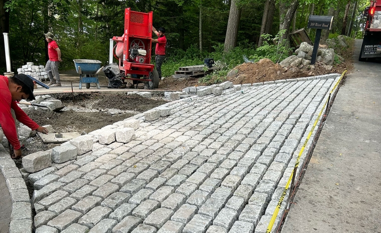 A man installs cobblestone edging on a brick walkway in Branford, CT, showcasing expert craftsmanship.