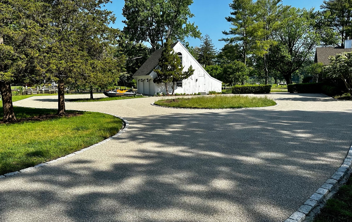 A white house with a circular cobblestone driveway in Chester, CT, framed by lush landscaping.