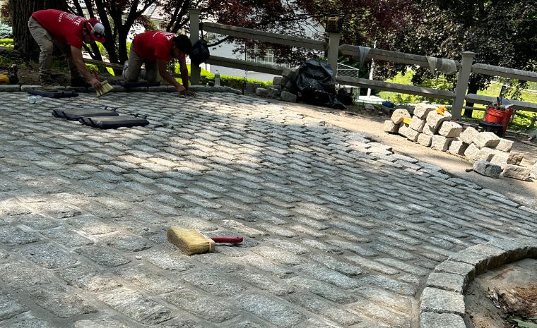 A man is constructing a brick patio, demonstrating custom finishes for a driveway apron in Mystic, CT.