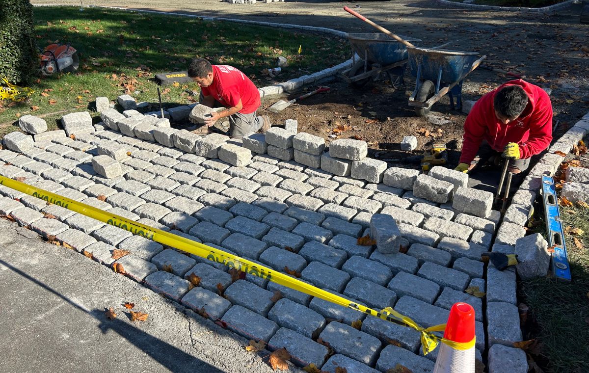 Two men are constructing a brick walkway at a driveway apron in Old Saybrook, CT.