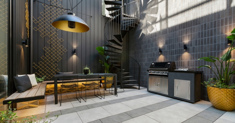 A modern outdoor kitchen featuring cooking areas, dining area and a spiral staircase, showcasing luxury patio design ideas.