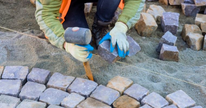 A man works on a brick walkway, demonstrating professional stone patio ideas for outdoor spaces.