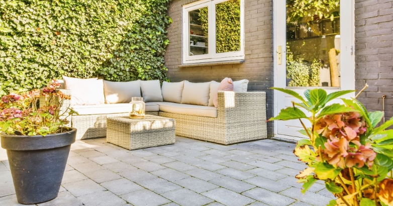 A modern minimalist stone patio featuring a couch and decorative potted plants, creating a stylish outdoor space.