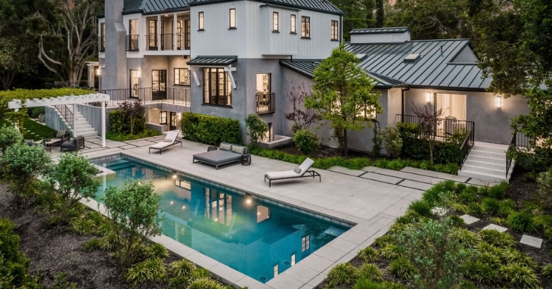 A spacious residence with a pool and a stylish stone patio, highlighting creative poolside stone patio designs.