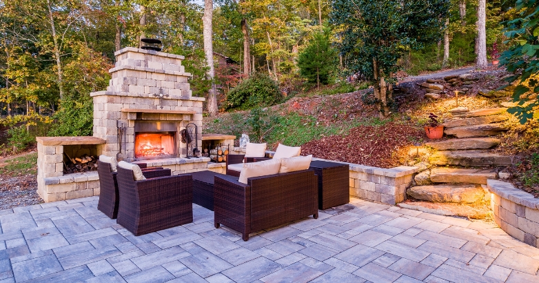 A stone patio featuring a built-in fireplace within a retaining wall, surrounded by comfortable seating for relaxation.