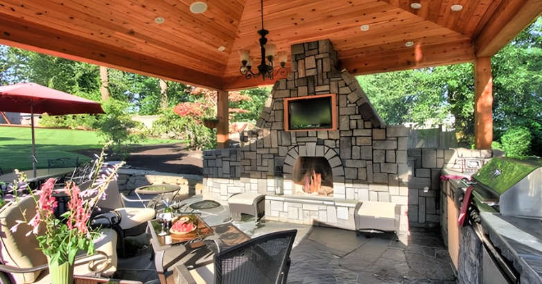 Outdoor living room featuring a cozy fireplace and an outdoor TV wall, perfect for entertaining and relaxation.