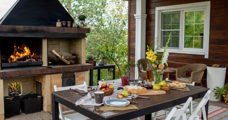 A patio table with chairs beside a fireplace, showcasing an integrated outdoor kitchen design.