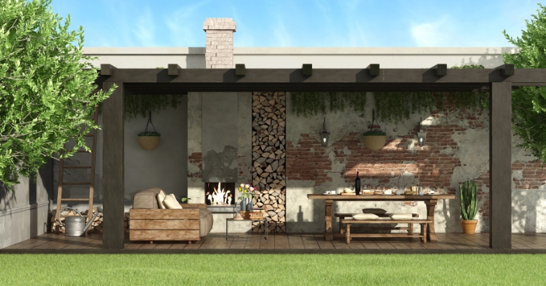 A cozy backyard with a wooden pergola and a table, designed for enjoying meals and warmth from a fireplace below.