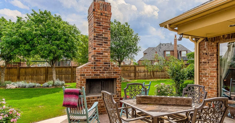 A cozy patio featuring a brick wood-burning fireplace with chimney and comfortable chairs for relaxation.
