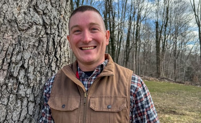 A man wearing a plaid vest stands next to a tree along a paver walkway in Essex, CT, highlighting a veteran-owned company.
