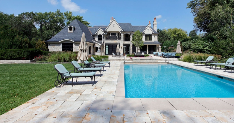 A spacious pool located in front of a house, highlighting considerations for choosing the right stone for pool decking.