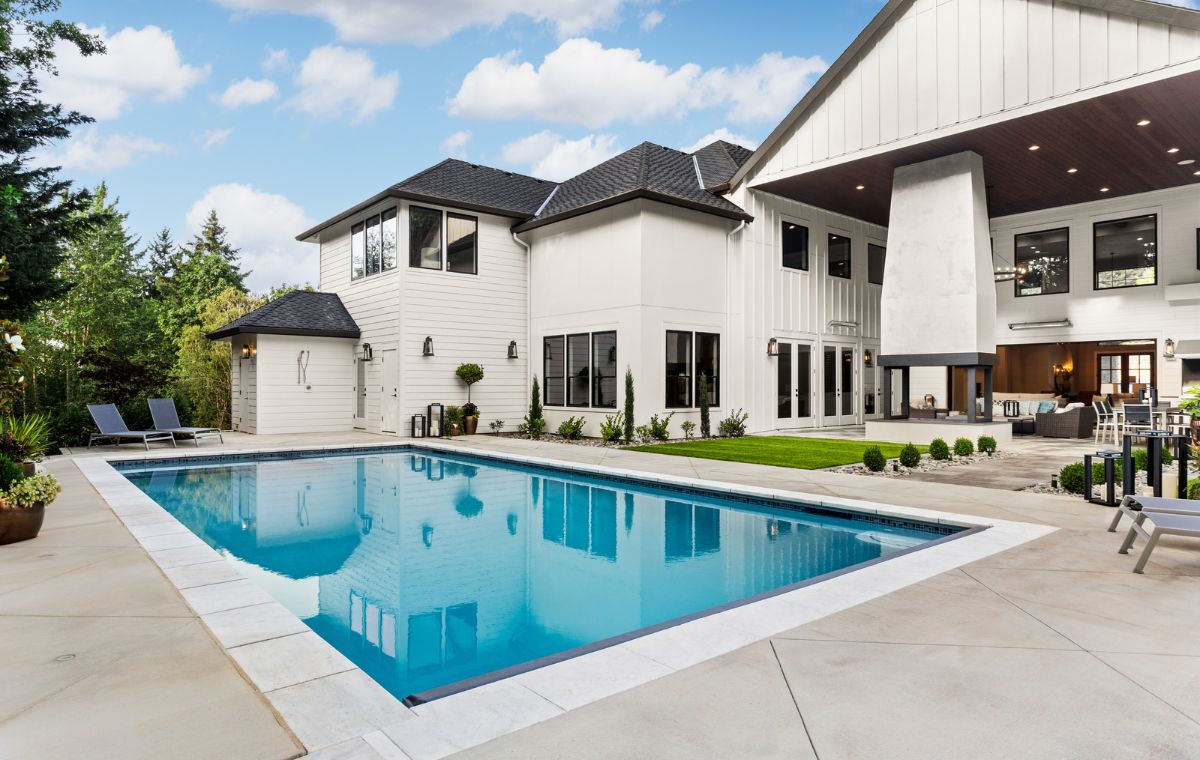 A prominent white residence with a pool and patio area, situated in Greenwich, CT, featuring stylish stone pool patios.