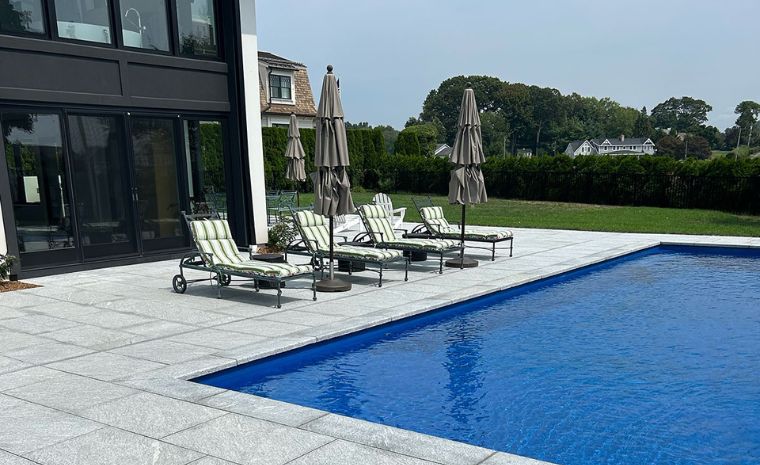A pool with lounge chairs and umbrellas in front of a house, showcasing a relaxing outdoor space in Greenwich, CT.