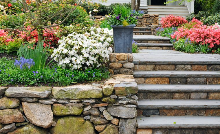 A charming stone pathway leads to a house, framed by blooming flowers, representing custom landscape design in Darien, CT.