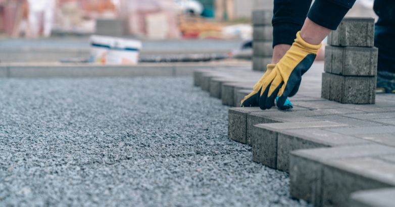 Worker installing concrete pavers on a gravel base during patio construction