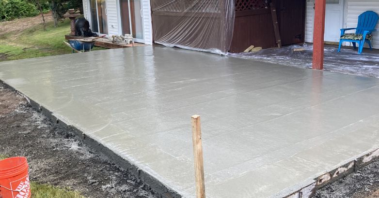 Freshly poured concrete patio slab being finished next to a house during outdoor construction project