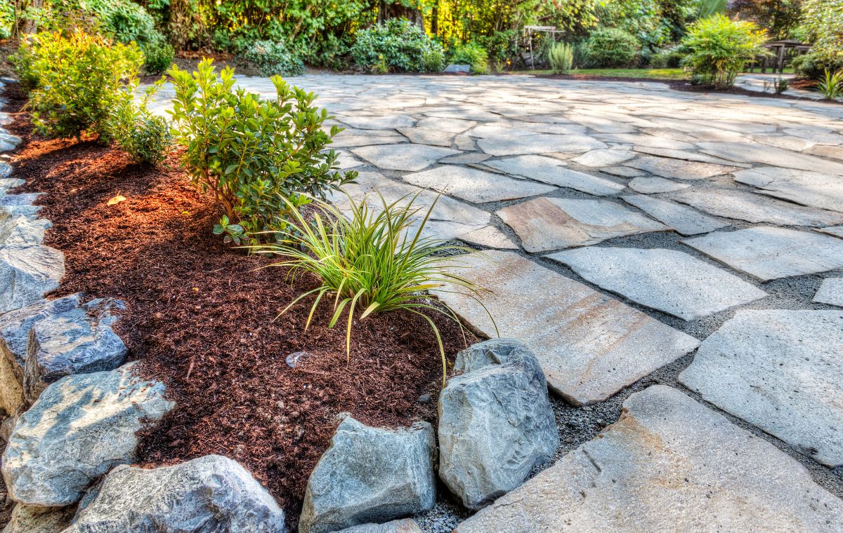 A beautifully arranged stone patio with vibrant plants and shrubs, featuring flagstone work in Madison, CT.
