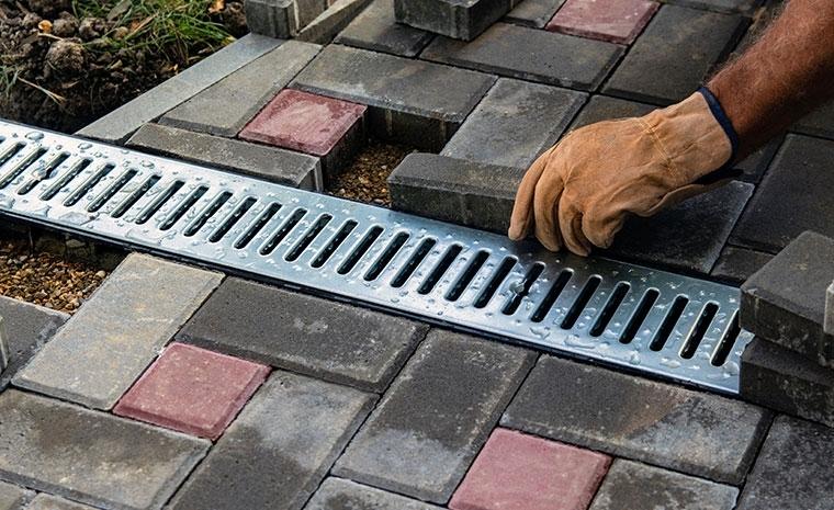 A man works on installing a drain in a brick walkway, part of drainage solutions for a front walkway in Branford, CT.