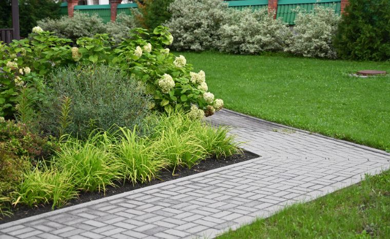 A charming brick path lined with shrubs, illustrating a paver walkway project by a Branford, CT contractor.