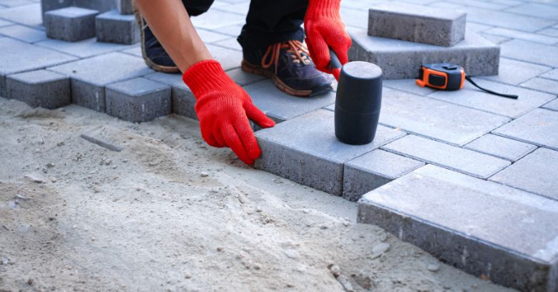 Worker installing interlocking concrete pavers on compacted sand base showing professional paver patio installation process.