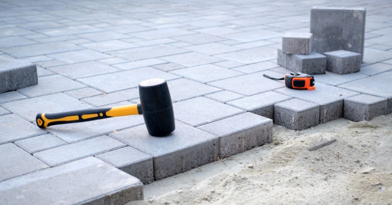 Concrete paver patio installation with rubber mallet and leveling tools showing base preparation and long-term investment quality.