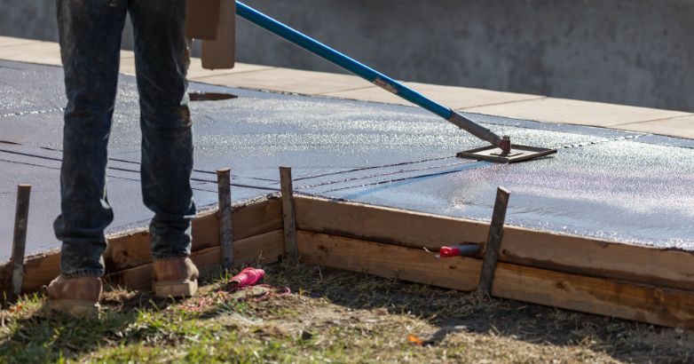 Concrete patio installation with worker leveling freshly poured slab during installation process and curing timeline.