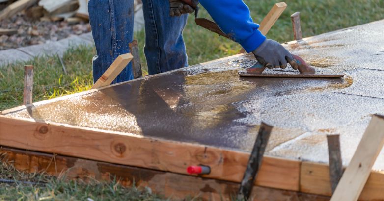 Worker finishing freshly poured concrete patio slab with hand trowel during professional concrete installation process.
