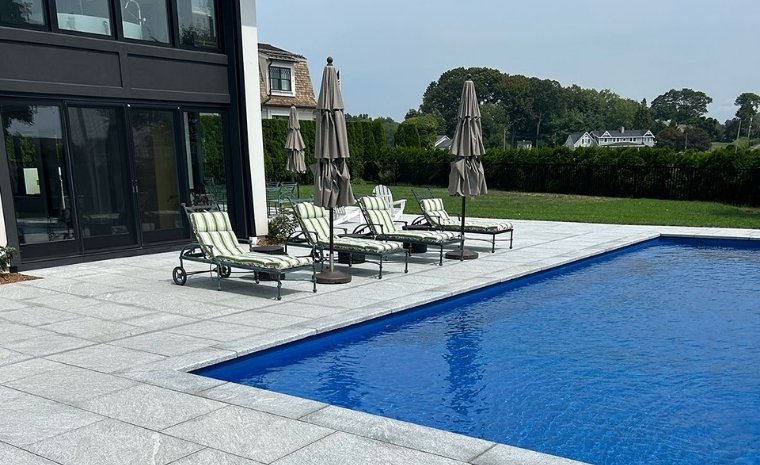 A residential pool area with lounge chairs and umbrellas, showcasing slip-resistant stone installation on the deck.