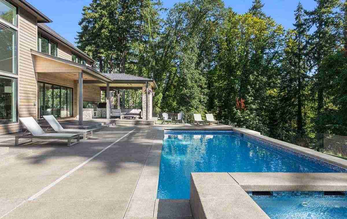 A modern home featuring a pool with a stone deck and patio, showcasing a stylish outdoor living space in Essex, CT.