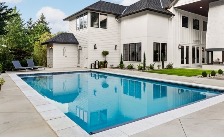A spacious white house with a pool and patio, highlighting the stone installation of the pool deck in Essex, CT.