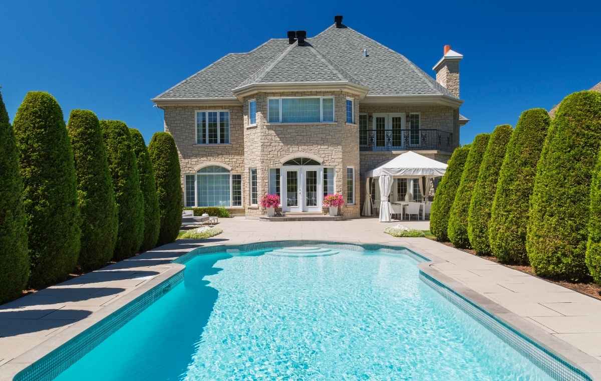 Exterior view of a spacious house featuring a pool and lawn, highlighting the stone pool deck installation in Stonington, CT.